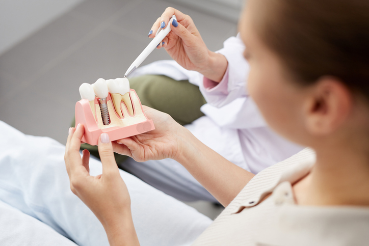 a woman holding a toothbrush and a model of a tooth.