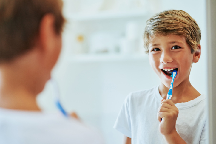 a young boy brushing his teeth in front of a mirror.